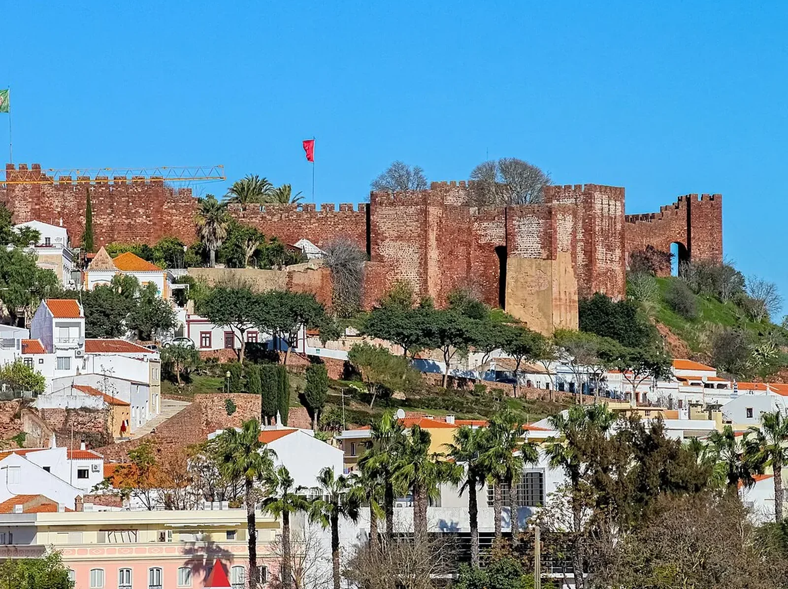 Het rode Moorse kasteel van Silves boven de witte huizen en palmen van de stad